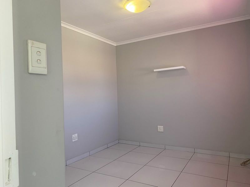 An empty bedroom featuring neutral grey walls, white tiled flooring, and a wall-mounted shelf, providing a clean and versatile space.