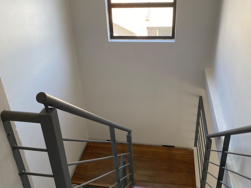 A bright staircase featuring timber treads, a modern metal balustrade, and a high-positioned window providing natural light to the landing area.