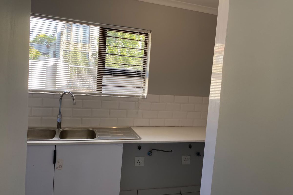 A clean, functional kitchen area featuring a double bowl stainless steel sink, subway tile backsplash, and white cabinetry with plumbing connections for appliances.