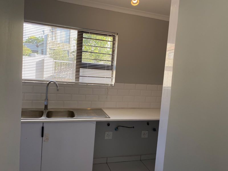 A clean, functional kitchen area featuring a double bowl stainless steel sink, subway tile backsplash, and white cabinetry with plumbing connections for appliances.