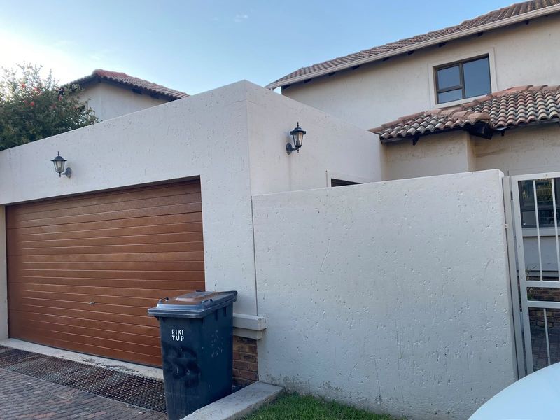 Front elevation of the townhouse featuring a wooden-look sectional garage door, tiled roof, and paved driveway access.