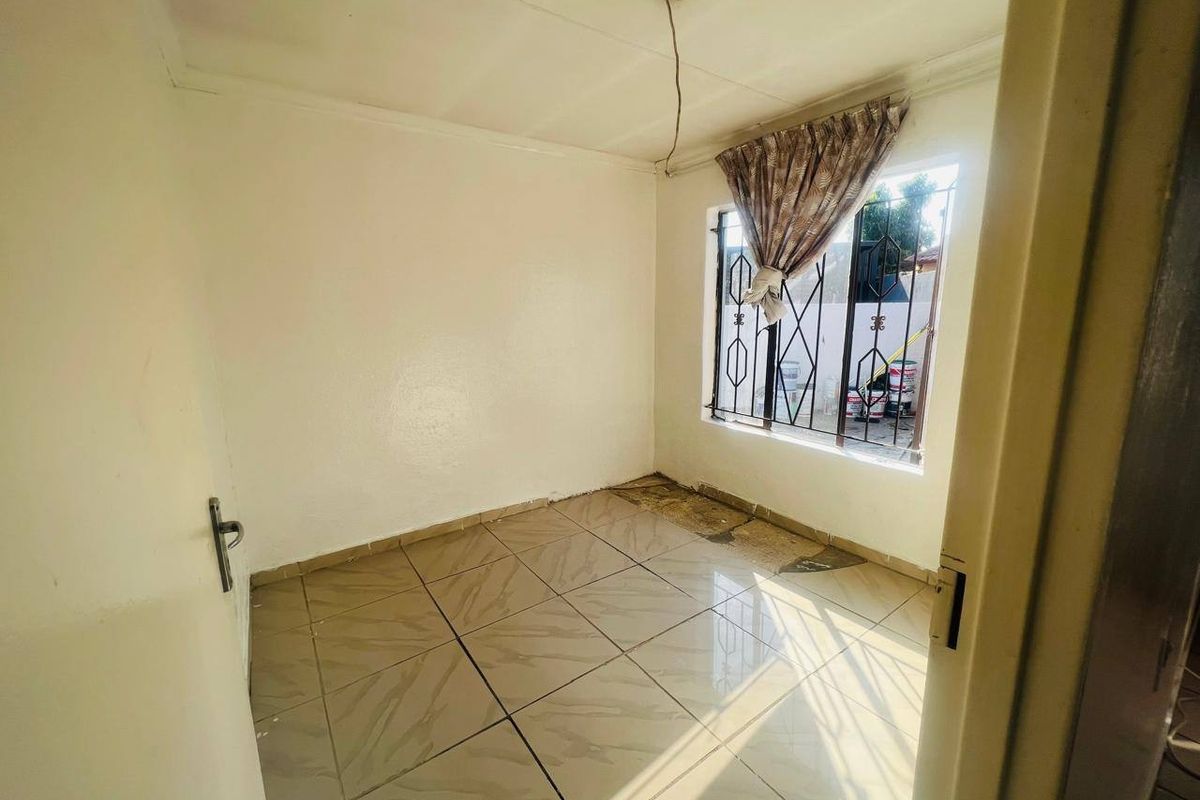 An empty bedroom featuring tiled flooring and security bars on the window, requiring minor repairs to the flooring and lighting.