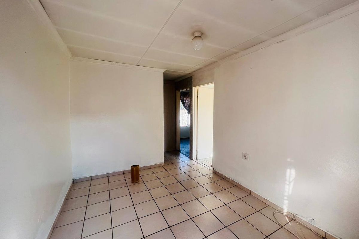 An empty living area featuring tiled flooring and ceiling tiles, offering a blank canvas for renovation and interior design updates.