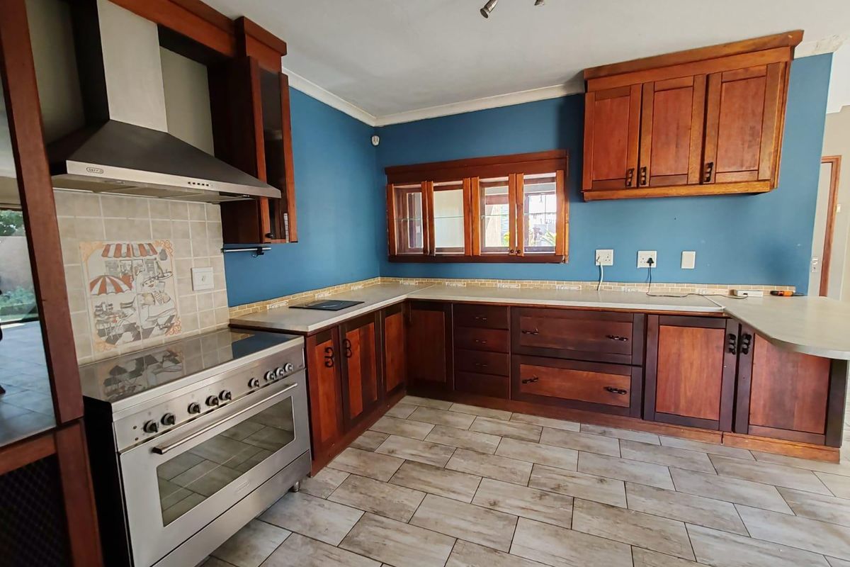 A spacious kitchen featuring dark wood cabinetry, stainless steel oven and extractor fan, tiled flooring, and a blue feature wall.