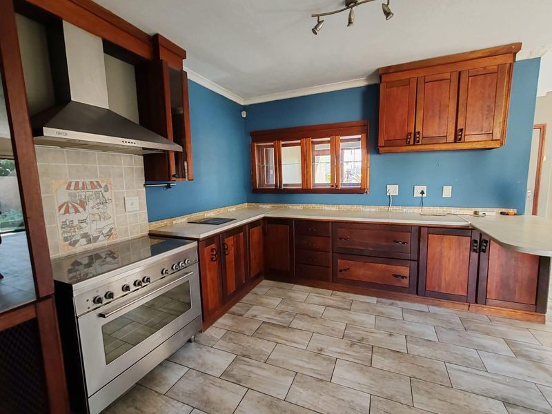 A spacious kitchen featuring dark wood cabinetry, stainless steel oven and extractor fan, tiled flooring, and a blue feature wall.