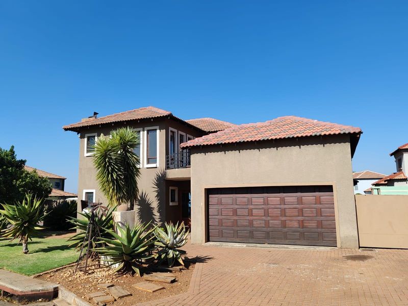 A well-maintained double-story residential house featuring a tiled roof, stucco exterior, and a paved driveway leading to a double garage.