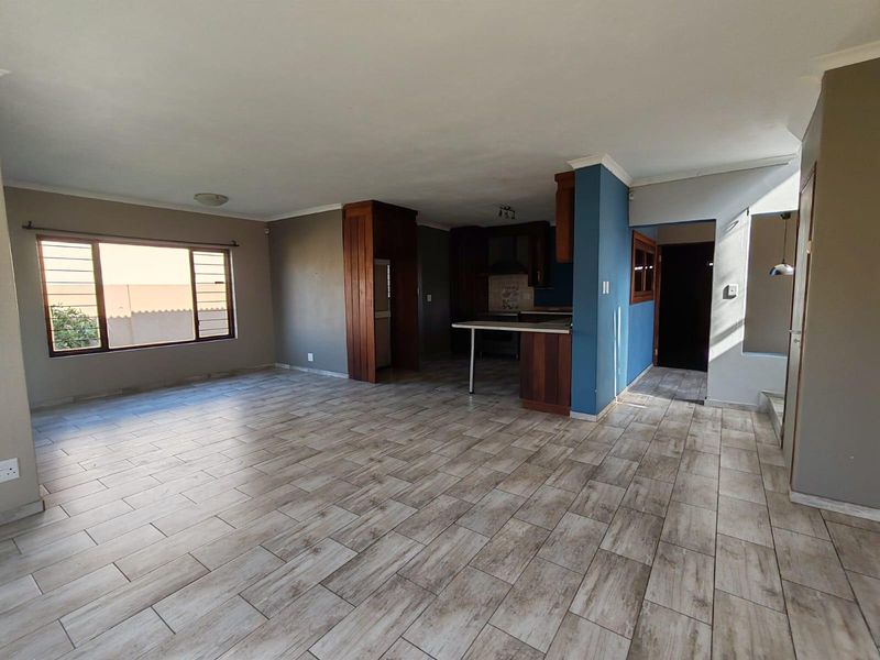 Spacious open-plan living area featuring modern wood-look tiled flooring and a functional kitchen with built-in cabinetry and a breakfast counter.