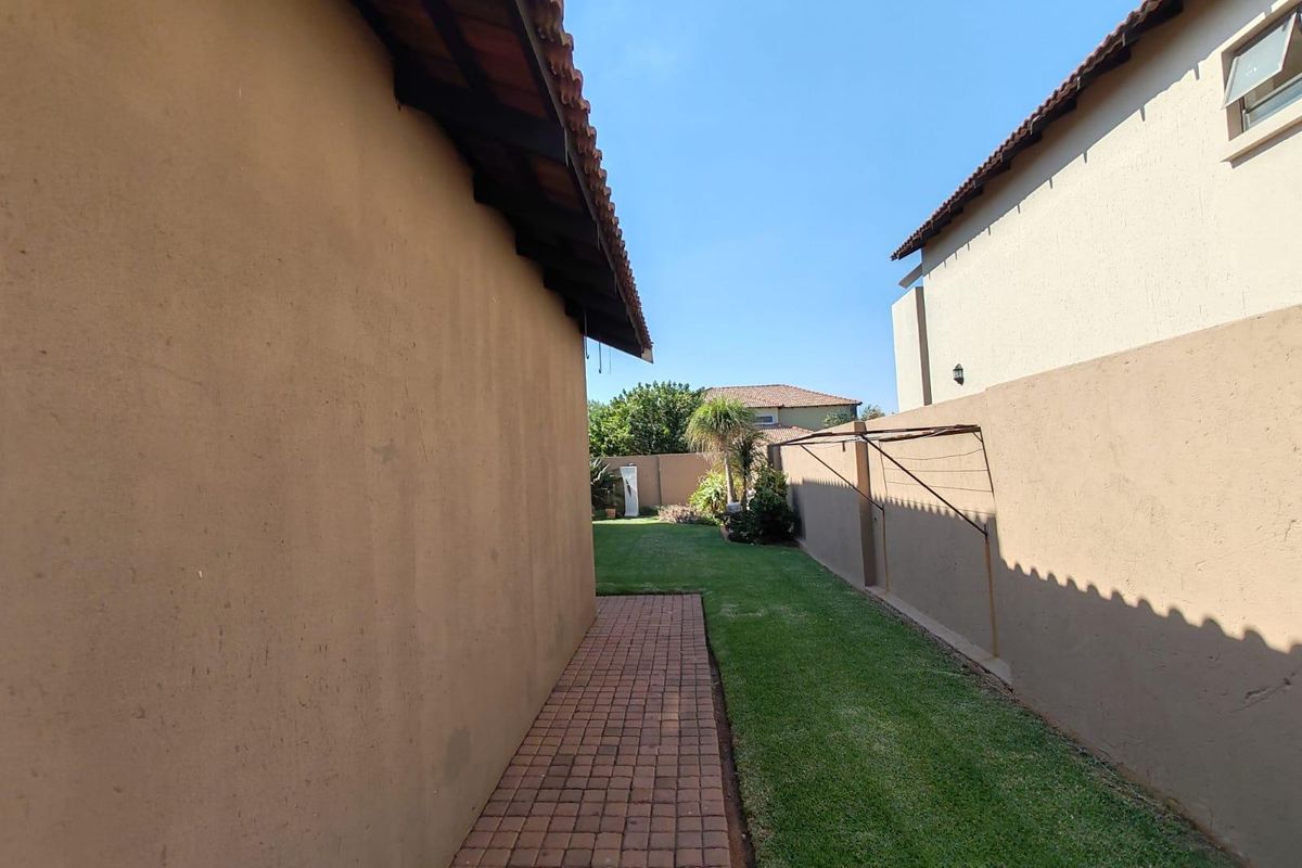 A side garden area featuring a paved walkway, manicured lawn, and high boundary walls between neighboring properties.
