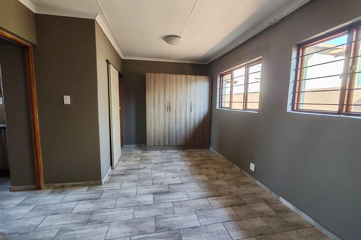 A clean, empty bedroom featuring modern wood-look floor tiles, a built-in wardrobe, and windows fitted with security bars.