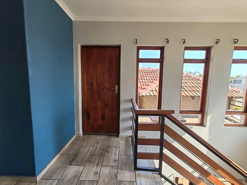 A bright landing area featuring tiled flooring, a solid wooden door, and a modern timber and metal staircase railing overlooking the lower level.