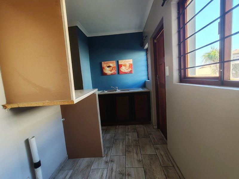 A functional scullery or utility area featuring tiled floors, built-in cabinetry with a stainless steel sink, and a window with security bars.