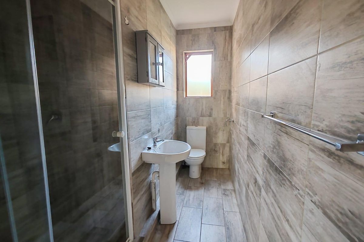 A modern bathroom featuring full-height wood-look wall tiling, a pedestal basin, a toilet, and a glass-enclosed shower.