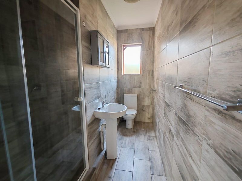 A modern bathroom featuring full-height wood-look wall tiling, a pedestal basin, a toilet, and a glass-enclosed shower.