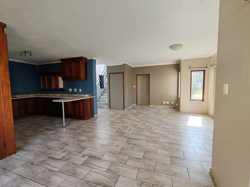 Spacious open-plan living area featuring tiled flooring, built-in wooden kitchen cabinetry, and a staircase leading to the upper level.