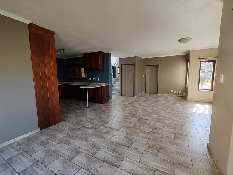 Spacious open-plan living area featuring tiled flooring, a functional kitchen with wooden cabinetry, and direct access to a staircase.