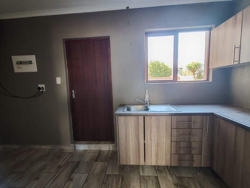 A functional kitchen area featuring wood-look laminate cabinetry, a stainless steel sink, and durable tiled flooring with an integrated electrical distribution board.