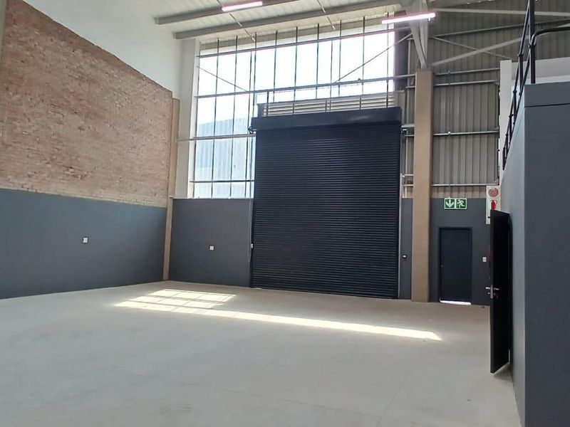 Spacious industrial warehouse unit featuring high ceilings, a large roller shutter door, concrete flooring, and a mezzanine level, ideal for storage or light manufacturing.