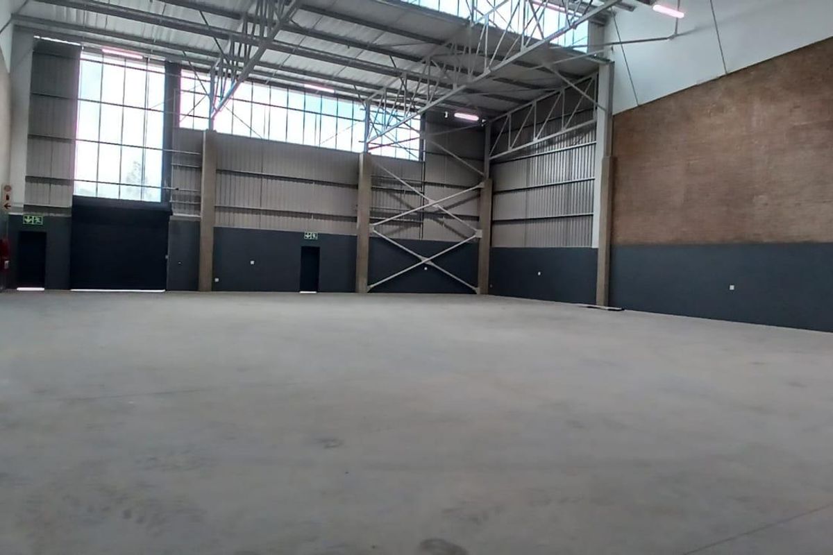 Spacious industrial warehouse unit featuring high ceilings, exposed steel trusses, concrete flooring, and large windows providing ample natural light.