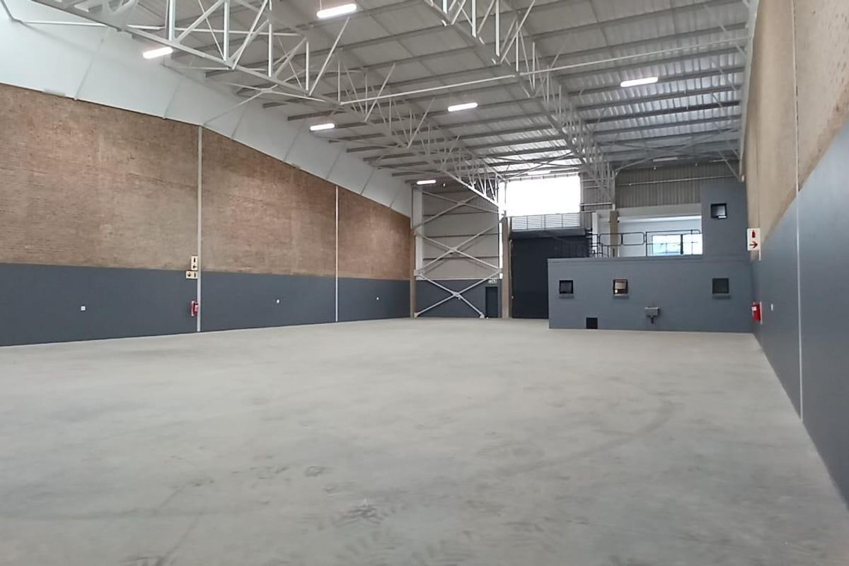 Spacious industrial warehouse featuring high ceilings with exposed steel trusses, concrete flooring, and a mezzanine level, suitable for various commercial or storage operations.