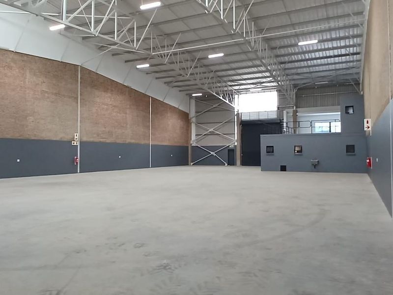 Spacious industrial warehouse featuring high ceilings with exposed steel trusses, concrete flooring, and a mezzanine level, suitable for various commercial or storage operations.
