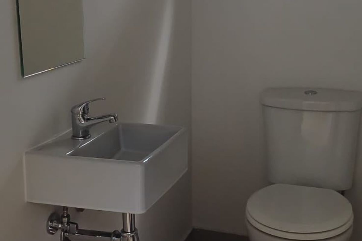 A clean and functional industrial-style bathroom featuring a wall-mounted basin, chrome fixtures, and a standard toilet.