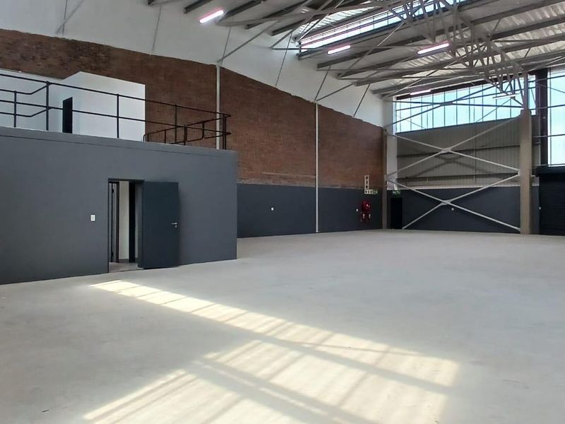 Spacious industrial warehouse featuring a mezzanine level, exposed brick walls, high steel roof trusses, and a large roller shutter door for easy access.