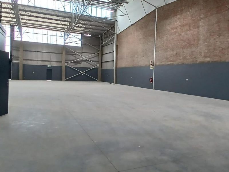 Spacious industrial warehouse unit featuring high ceilings with exposed steel trusses, concrete flooring, and a combination of brick and painted wall finishes.