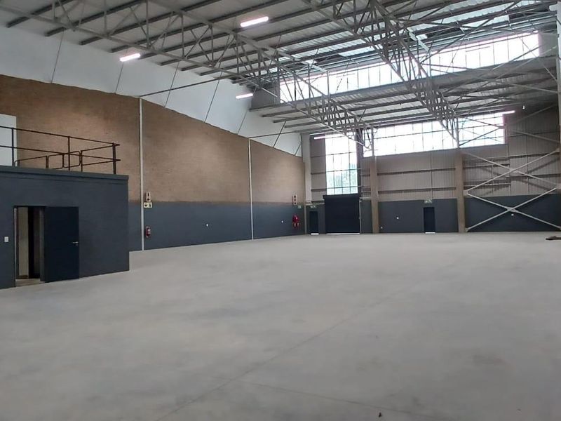 Spacious industrial warehouse featuring high ceilings with exposed steel trusses, polished concrete flooring, a mezzanine level, and large roller shutter access.