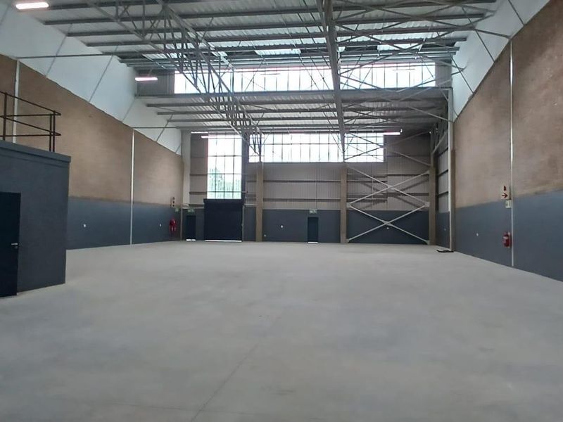 Spacious industrial warehouse unit featuring high ceilings with exposed steel trusses, concrete flooring, and a mezzanine level, suitable for various commercial or storage uses.