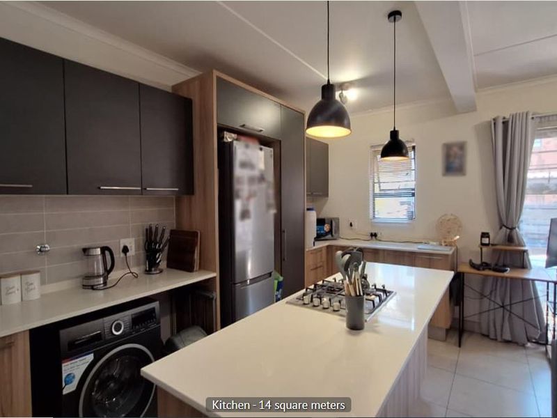 Modern open-plan kitchen featuring dark and wood-tone cabinetry, stone countertops, a central island with a gas hob, and integrated laundry appliances.