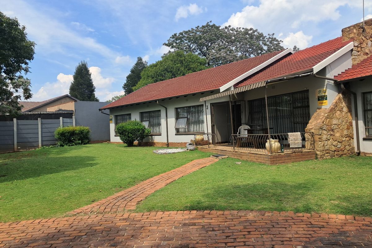 Rear view of the house featuring a covered patio, stone cladding accents, a tiled roof, and a spacious lawn with a brick-paved walkway.