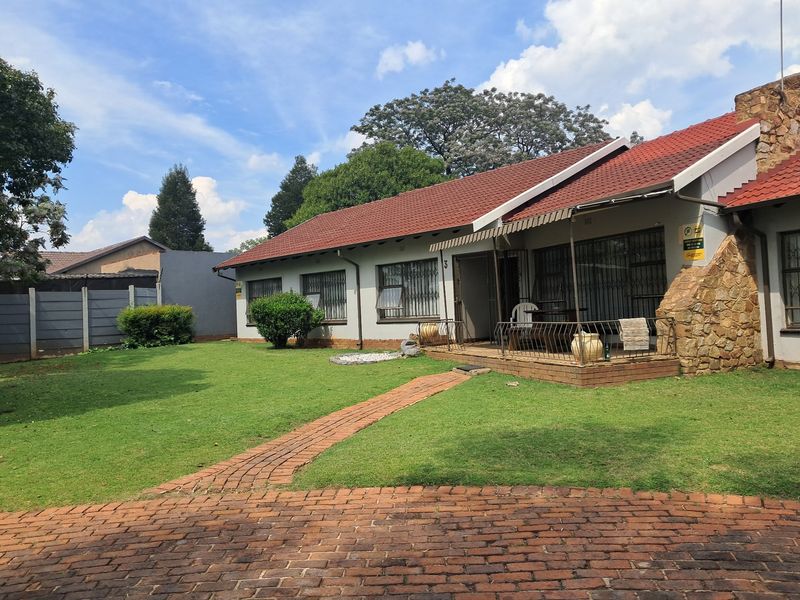 Rear view of the house featuring a covered patio, stone cladding accents, a tiled roof, and a spacious lawn with a brick-paved walkway.