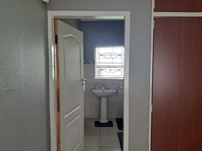 A view through a doorway into a functional bathroom featuring a pedestal basin, tiled floors, and security bars on the window.