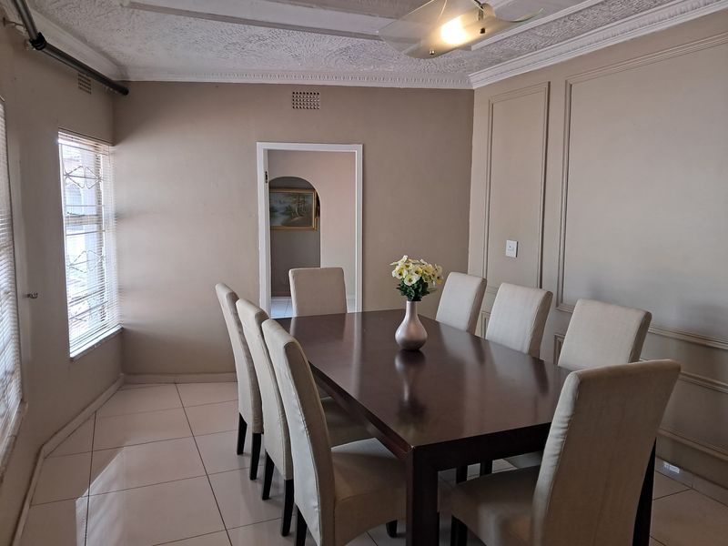 A dining room featuring tiled flooring, decorative ceiling cornices, and wall paneling, with security bars installed on the windows.