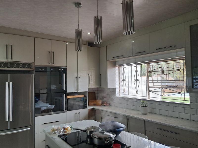 Modern kitchen featuring high-gloss cabinetry, stone countertops, subway tile backsplash, and integrated appliances, complemented by stylish pendant lighting and a window with security bars.
