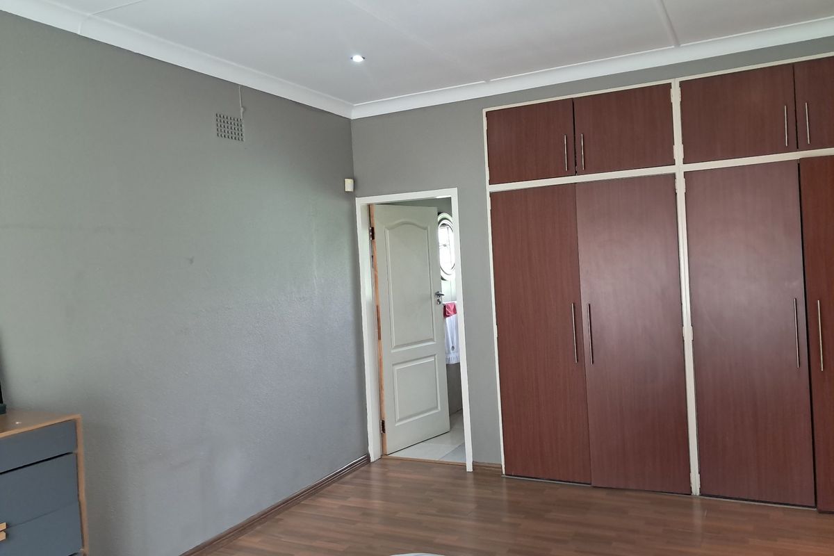 A spacious bedroom featuring dark wood built-in cupboards, laminate flooring, and neutral grey walls, offering a clean and functional living space.