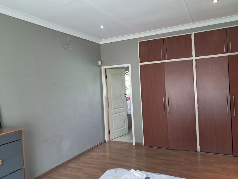 A spacious bedroom featuring dark wood built-in cupboards, laminate flooring, and neutral grey walls, offering a clean and functional living space.