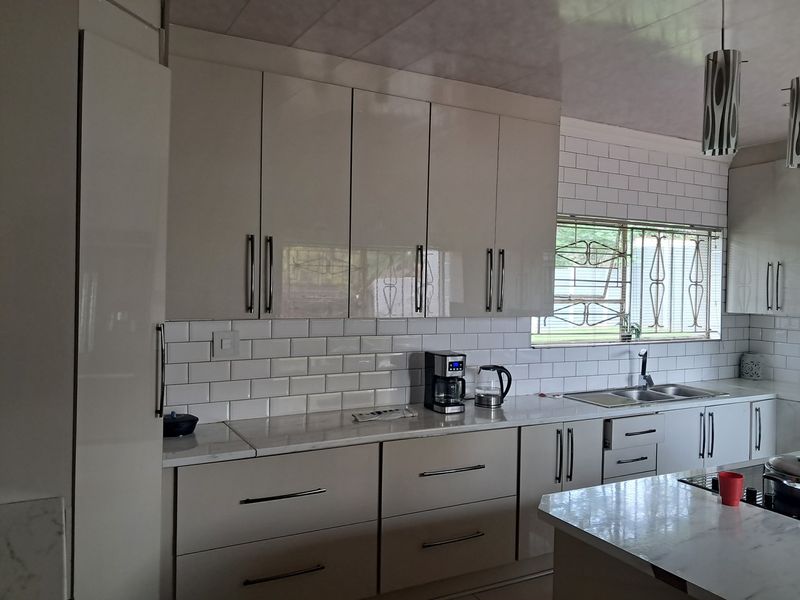 Modern kitchen featuring high-gloss cabinetry, marble countertops, and a classic subway tile backsplash with ample storage and a double basin sink.