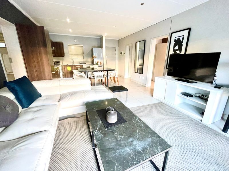 An open-plan living and kitchen area featuring tiled flooring, recessed lighting, and modern kitchen cabinetry in a well-maintained apartment setting.