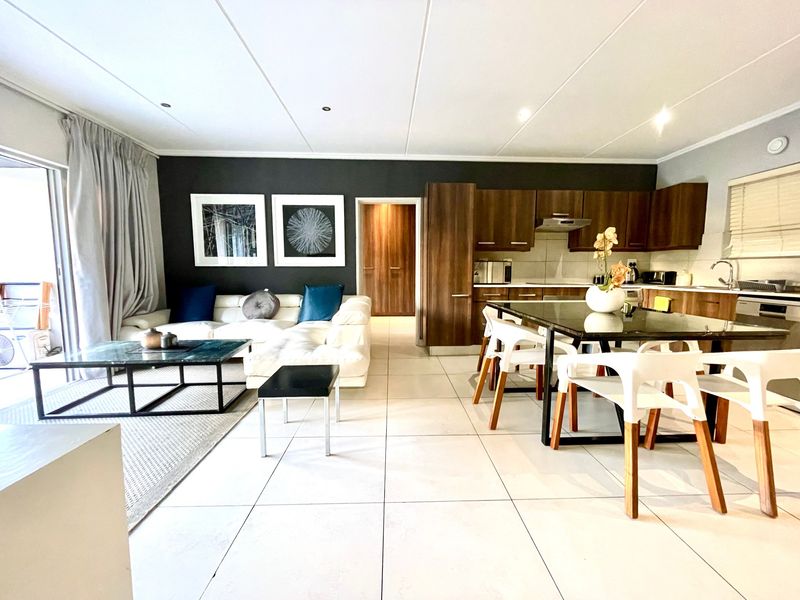 Open-plan living and kitchen area featuring tiled flooring, modern dark wood cabinetry, and a sliding door leading to an outdoor space.