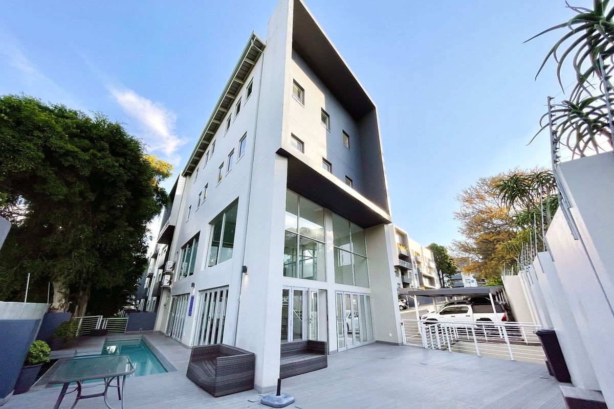 Modern apartment building exterior featuring a rear deck area with a swimming pool, large glass windows, and contemporary architectural design.