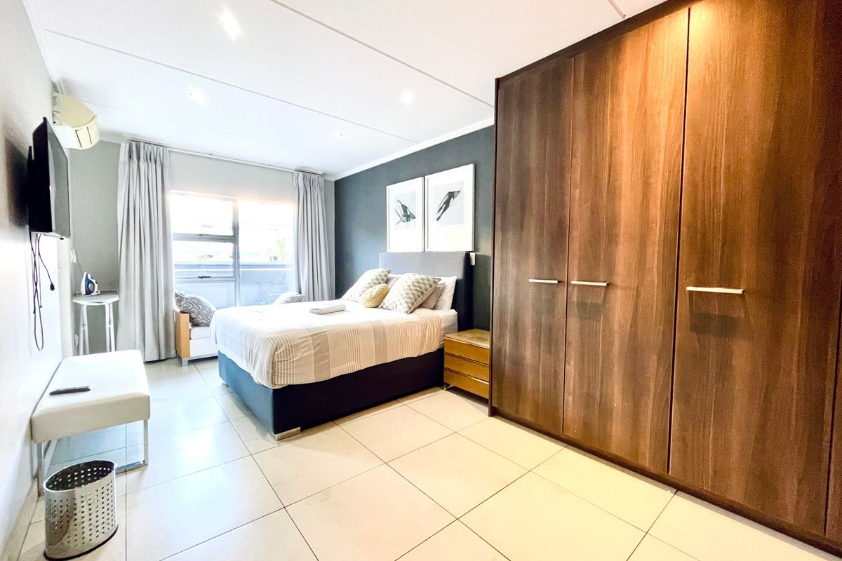 A well-maintained bedroom featuring large built-in wooden wardrobes, tiled flooring, recessed lighting, and a wall-mounted air conditioning unit.