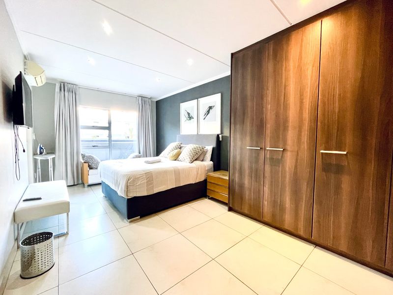 A well-maintained bedroom featuring large built-in wooden wardrobes, tiled flooring, recessed lighting, and a wall-mounted air conditioning unit.