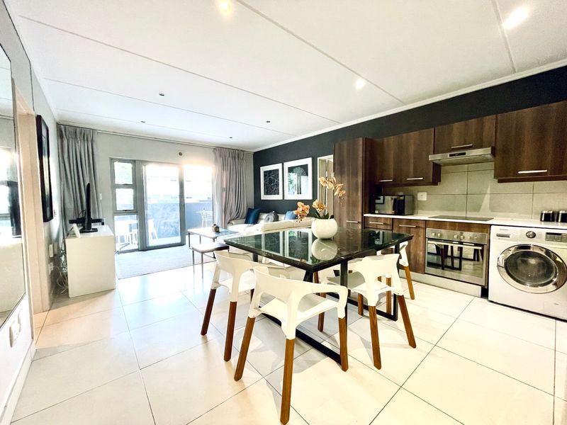Modern open-plan living area featuring a contemporary kitchen with built-in cabinetry, integrated appliances, and seamless flow to a private balcony through sliding glass doors.
