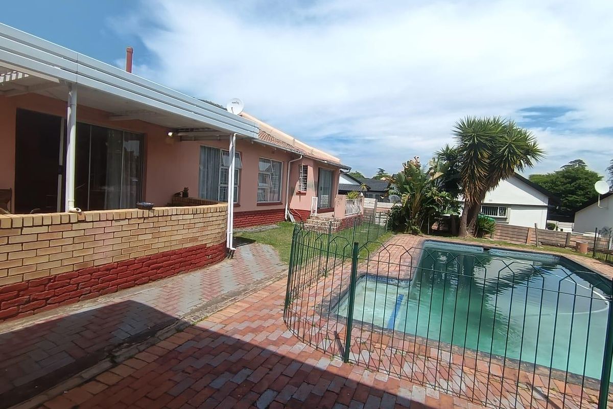 Rear exterior view featuring a swimming pool with safety fencing, paved patio area, and covered veranda attached to the main house structure.