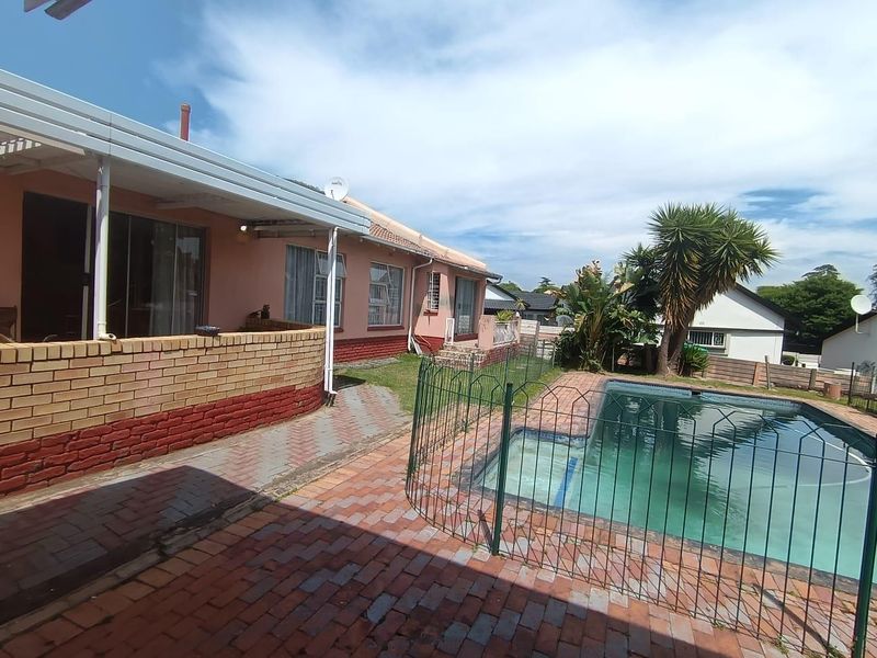 Rear exterior view featuring a swimming pool with safety fencing, paved patio area, and covered veranda attached to the main house structure.