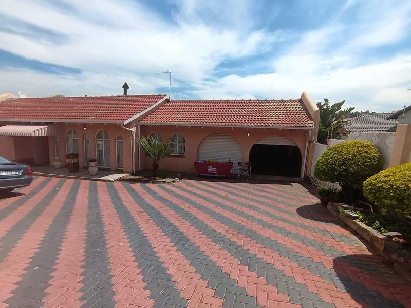 Front exterior view of a single-story house featuring a patterned paved driveway, arched garage openings, and a tiled roof.