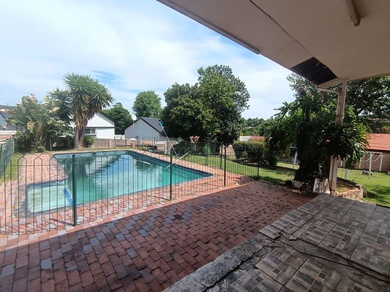 Outdoor entertainment area featuring a swimming pool with safety fencing, brick paving, and a covered patio space.