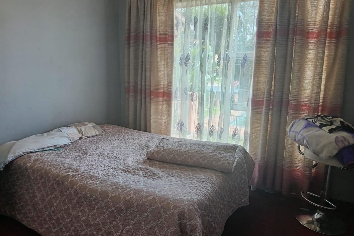 A standard bedroom featuring a large window with floor-to-ceiling curtains, providing natural light and a view of the exterior.