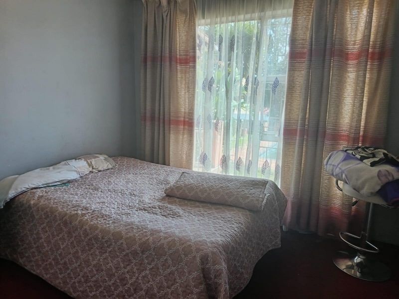 A standard bedroom featuring a large window with floor-to-ceiling curtains, providing natural light and a view of the exterior.